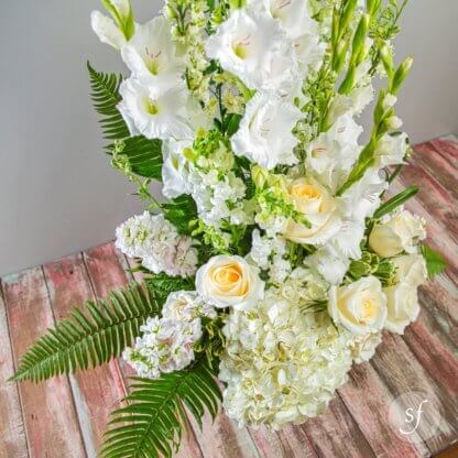 Express sympathy with this large and elegant funeral arrangement featuring white gladioli, roses, hydrangea, and snapdragons in a black urn.