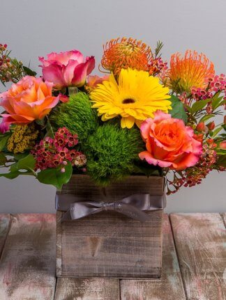 The Brighten Your Day arrangement is a sweet fall arrangement featuring colorful blooms in a rustic box base.